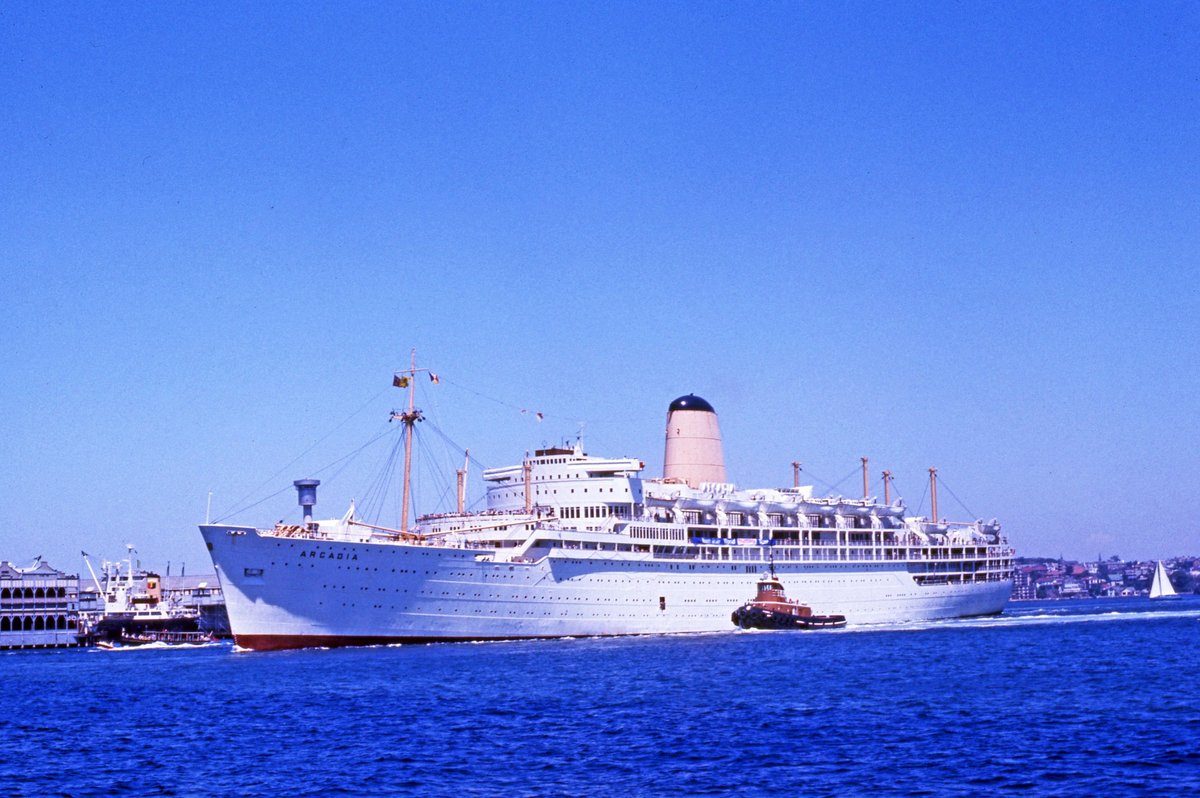 P & O Liner Arcadia & two tugs passing a cargo ship at a wharf just west of Harbour Bridge Sydney (1975)