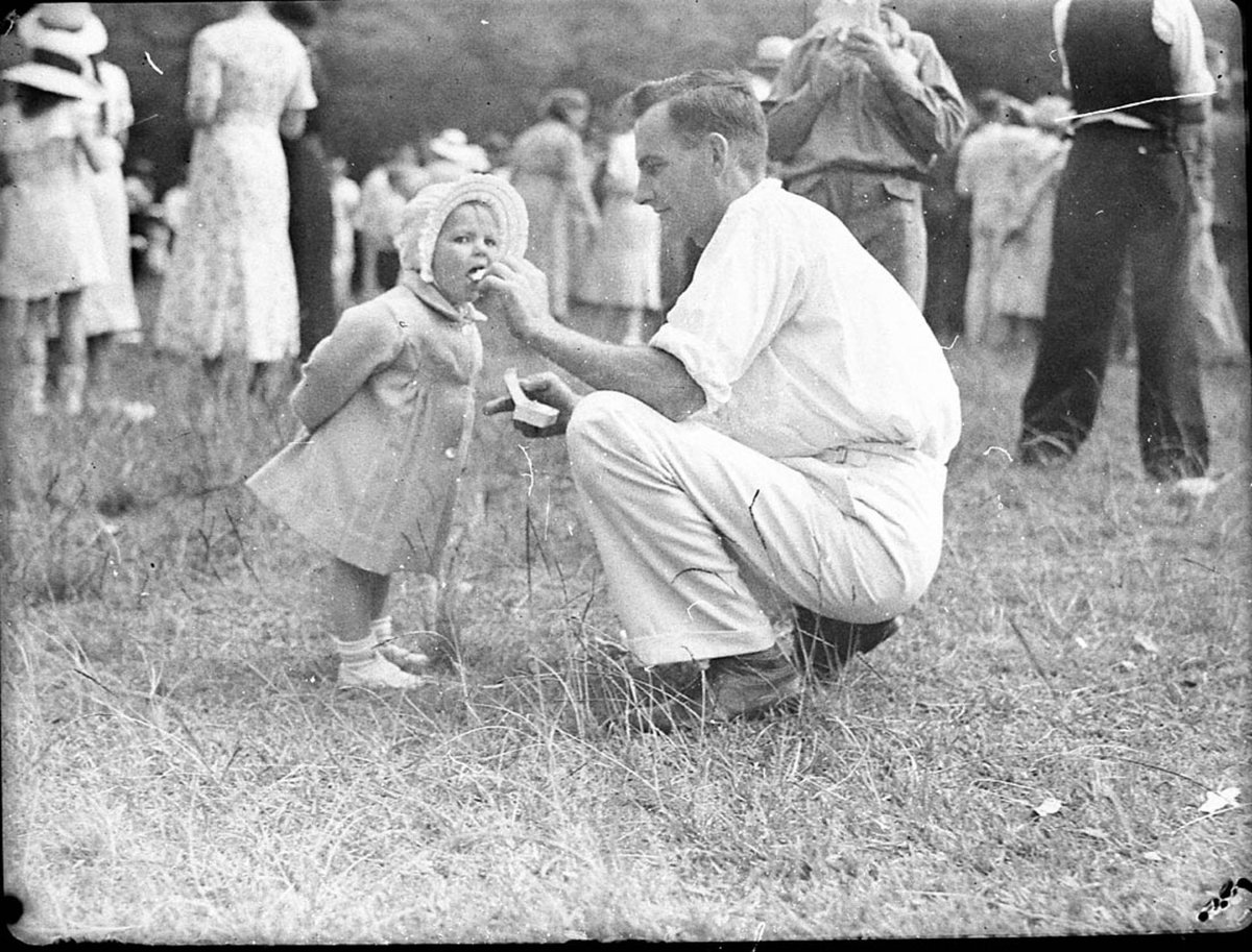 A man feeding a baby icecream Australian Paper Mills picnic at Clifton Gardens, Mosman (1935)