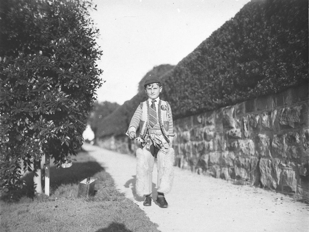 A schoolboy wearing cowboy chaps and vest over his school uniform (1930s)