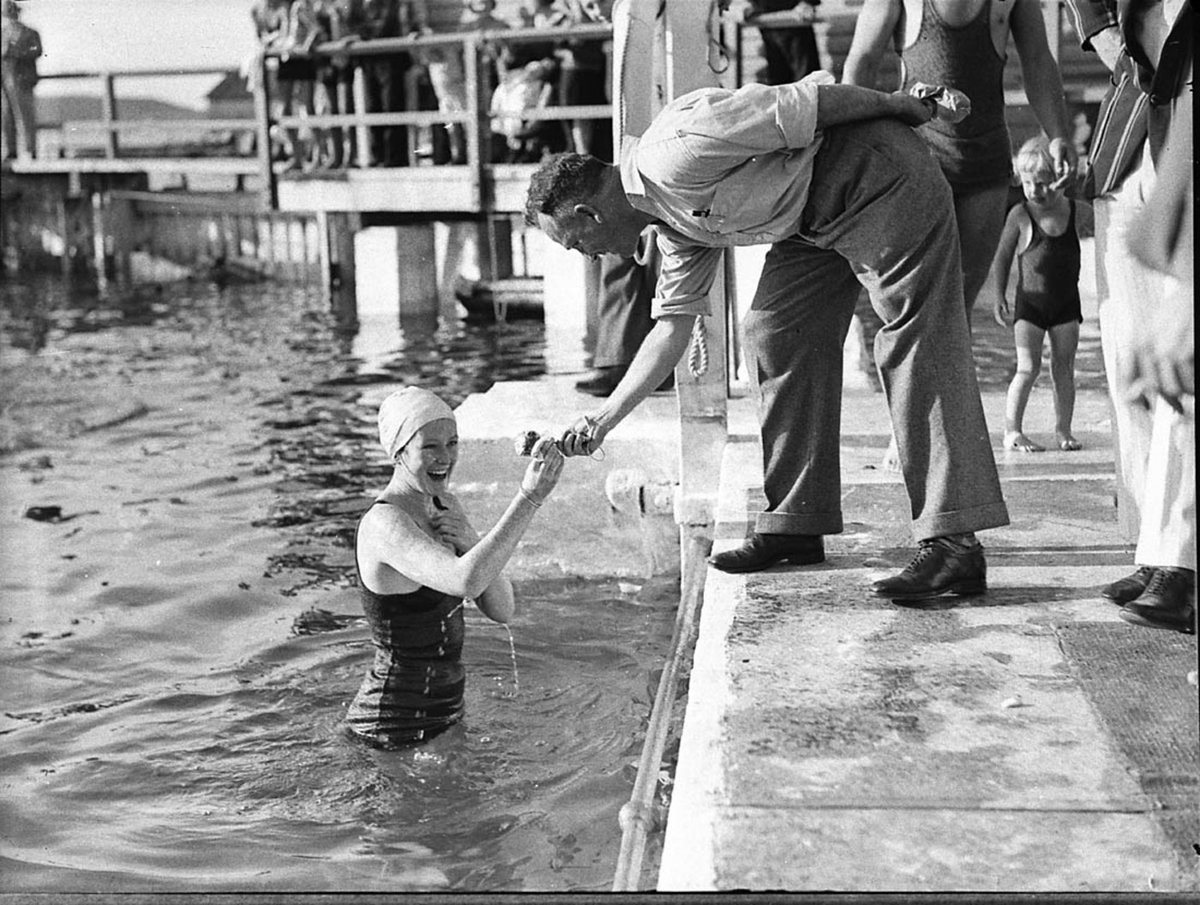 An official hands a young woman swimmer a token Tramway swimming at Coogee Aquarium (1935)