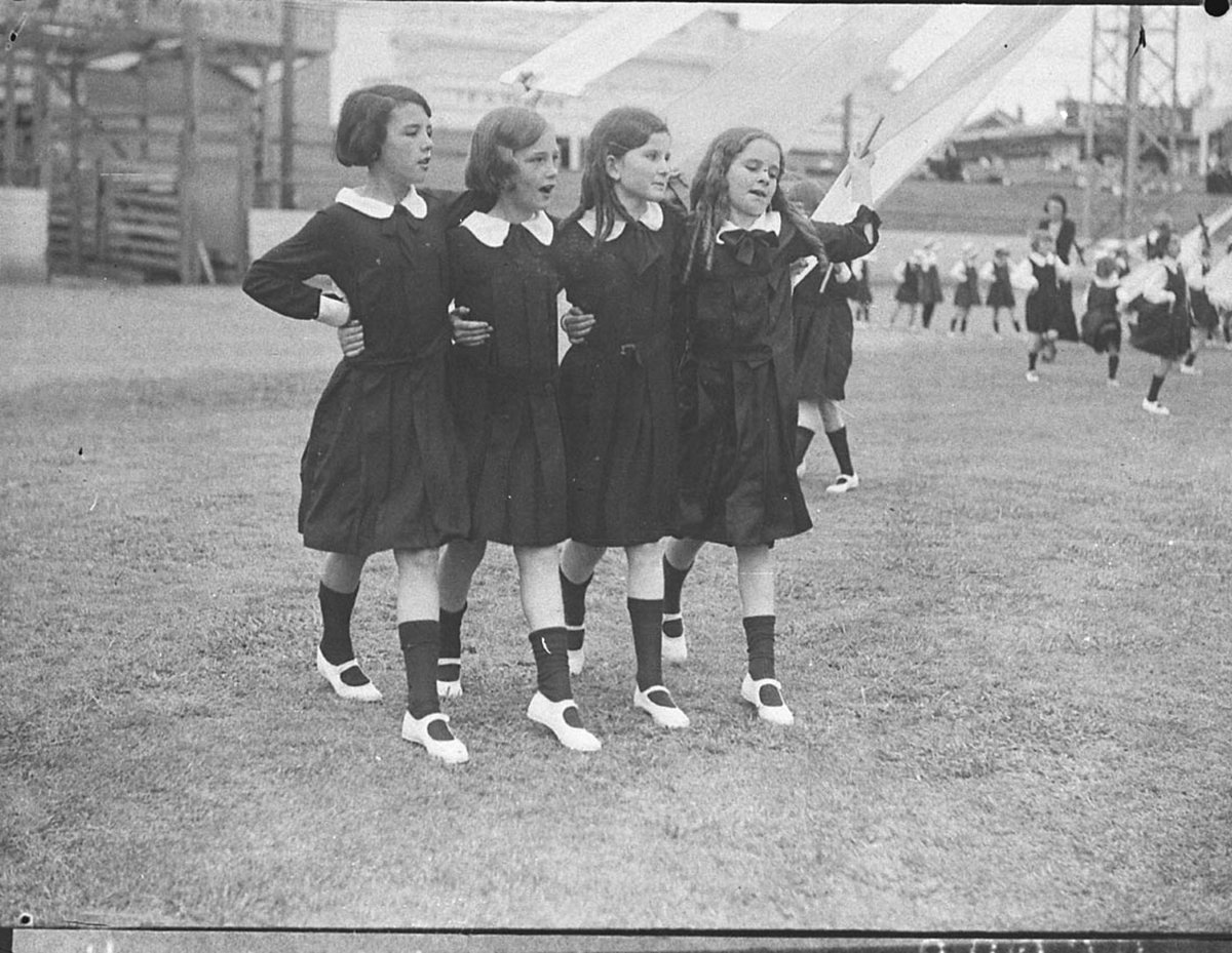 Group of four young schoolgirls singing as they dance round the maypole (1935)