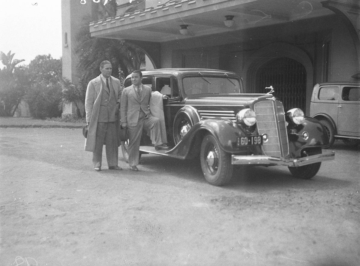 Joe Kirkwood and friend and 1932 Buick outside the Conservatorium, Sydney city centre (1930s)
