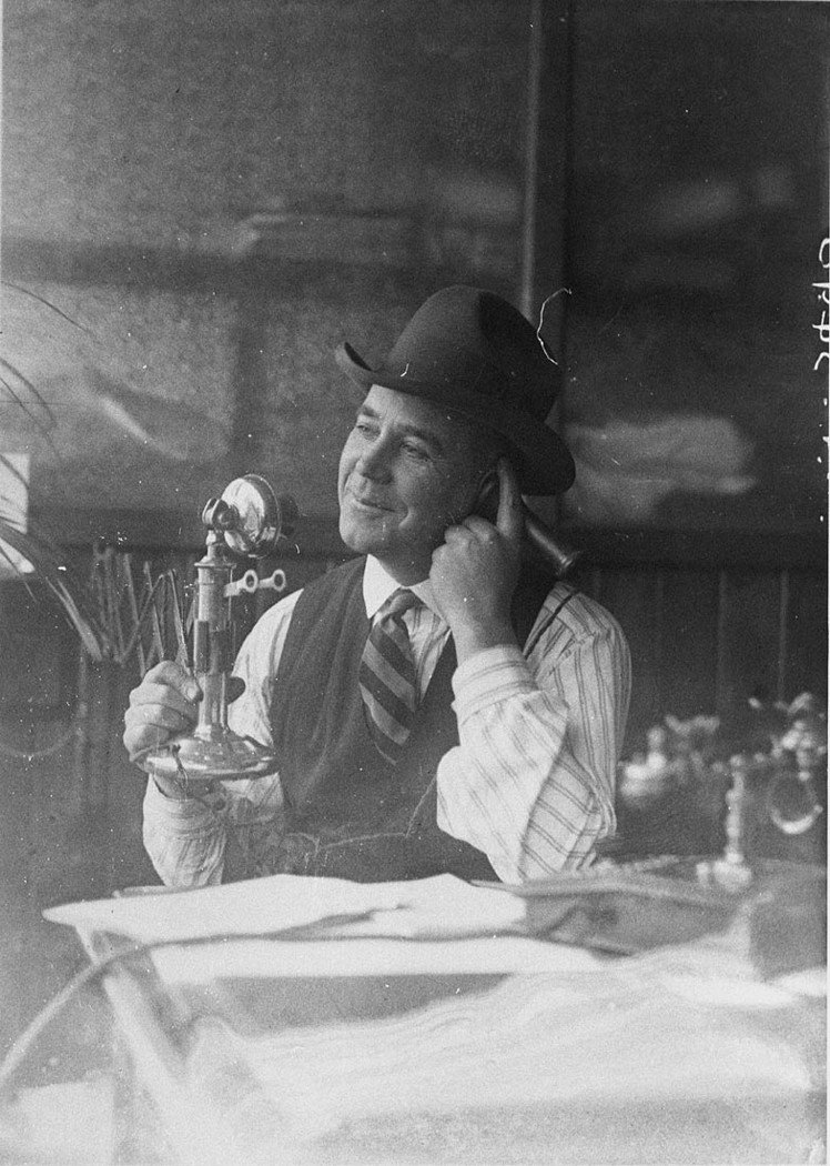 Man wearing Stetson hat talking on candlestick telephone (c. 1931)