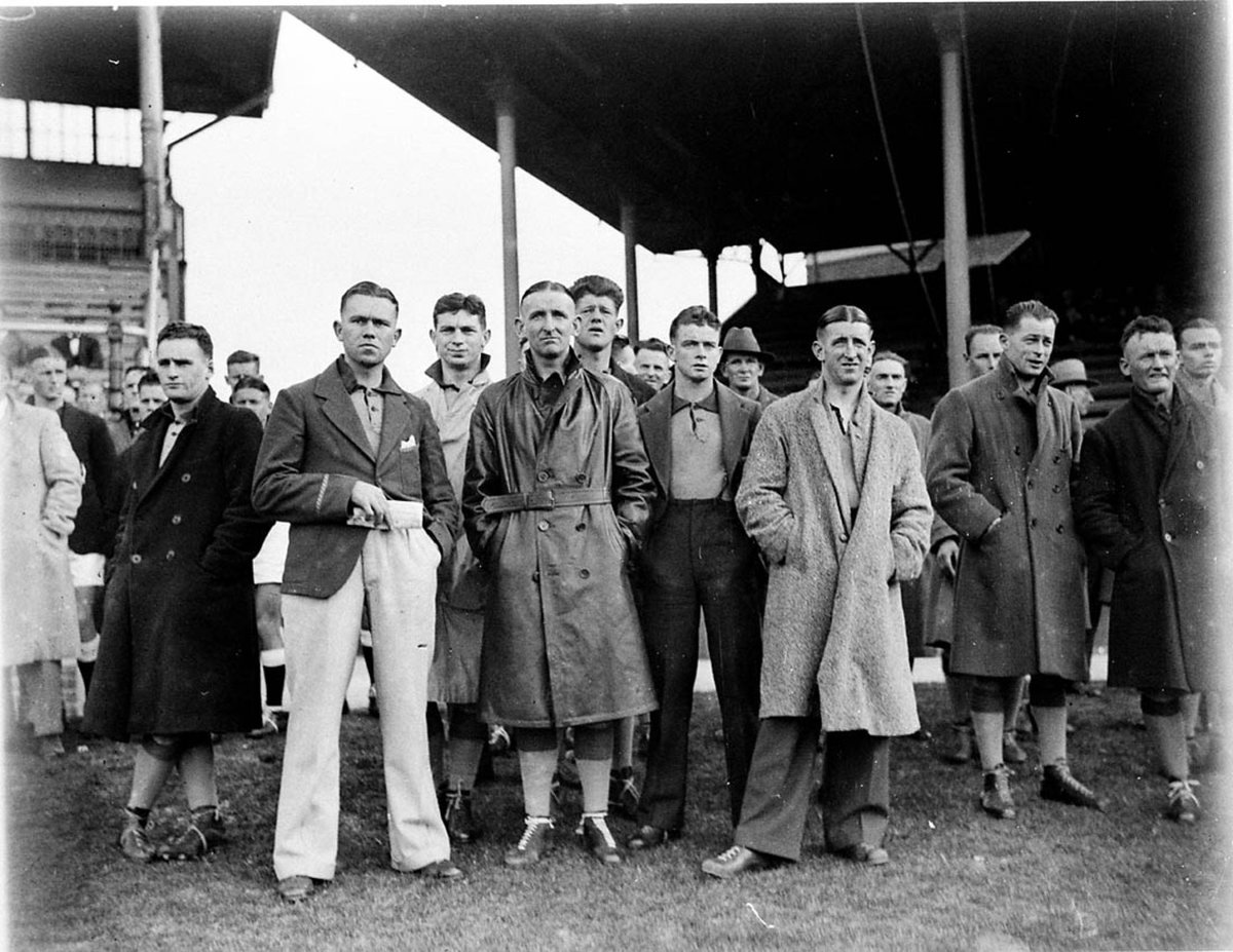 Members of the Canberra team wait for their game against NSW in the AllStates Australian Football Carnival at the SCG on 7 August 193 the player in the leather coat centre is the teams captain Jack Moroney, Moore Park (1933)