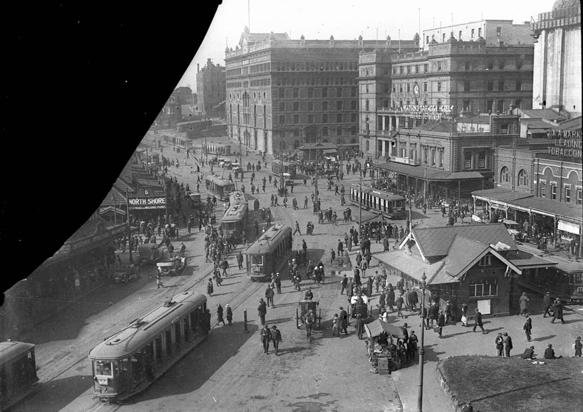 Scene of Circular Quay showing trams two hansom cabs old touring cars fruit barrows Goldsbrough Mort Building North Shore ferry wharf Steamers for Milsons Point McMahons Point and Lavender Bay wharf (1930s)
