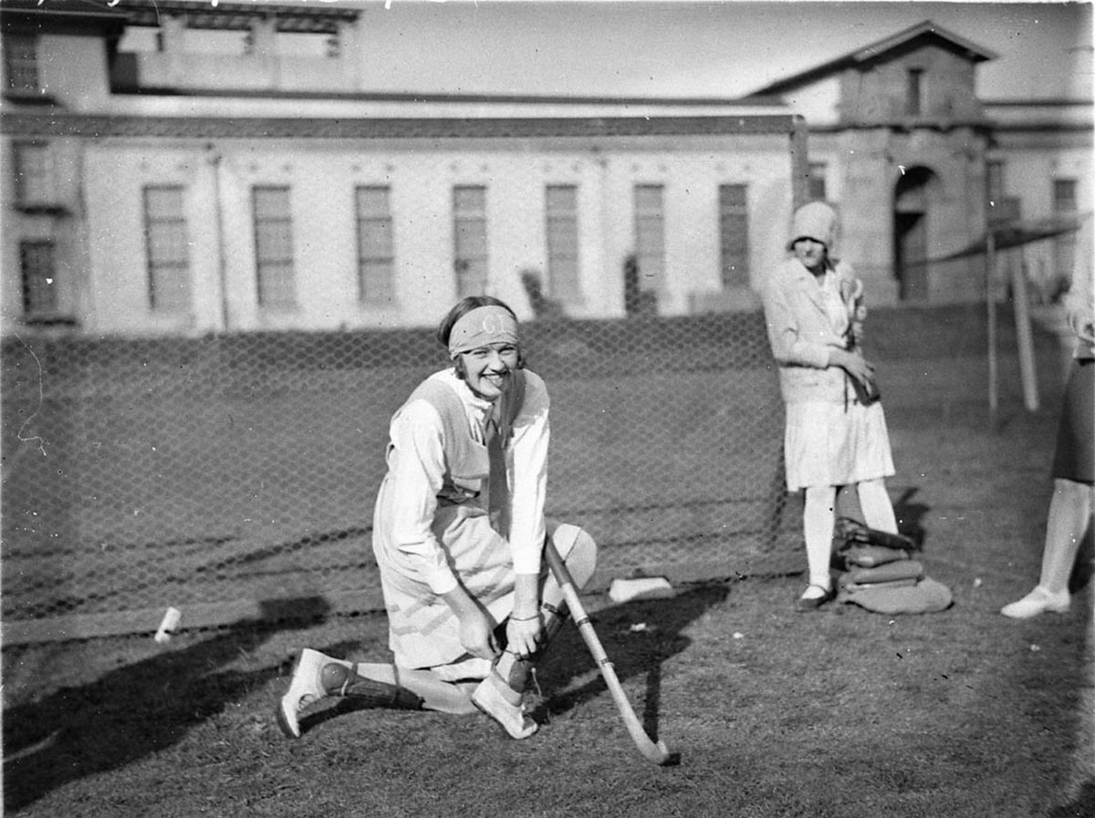 Schoolgirl hockey goalie adjusting her shin pads (1929)