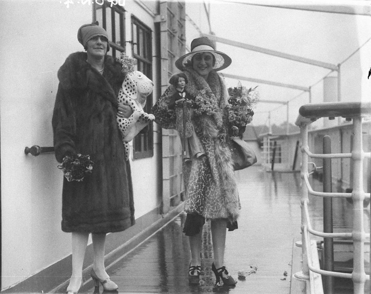 Two unidentified JCW actresses or singers in fur coats with toy dog and doll on deck of a ship (1927–30)