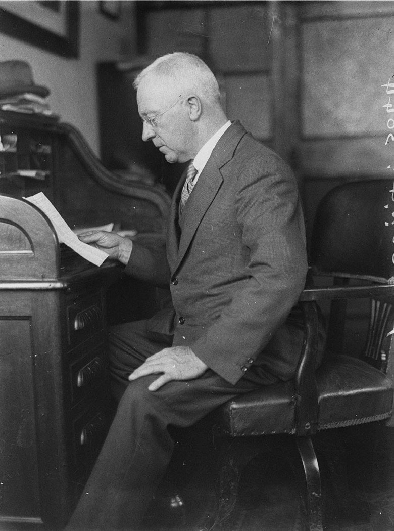 Unidentified man reading document sitting at rolltop desk (1930s)