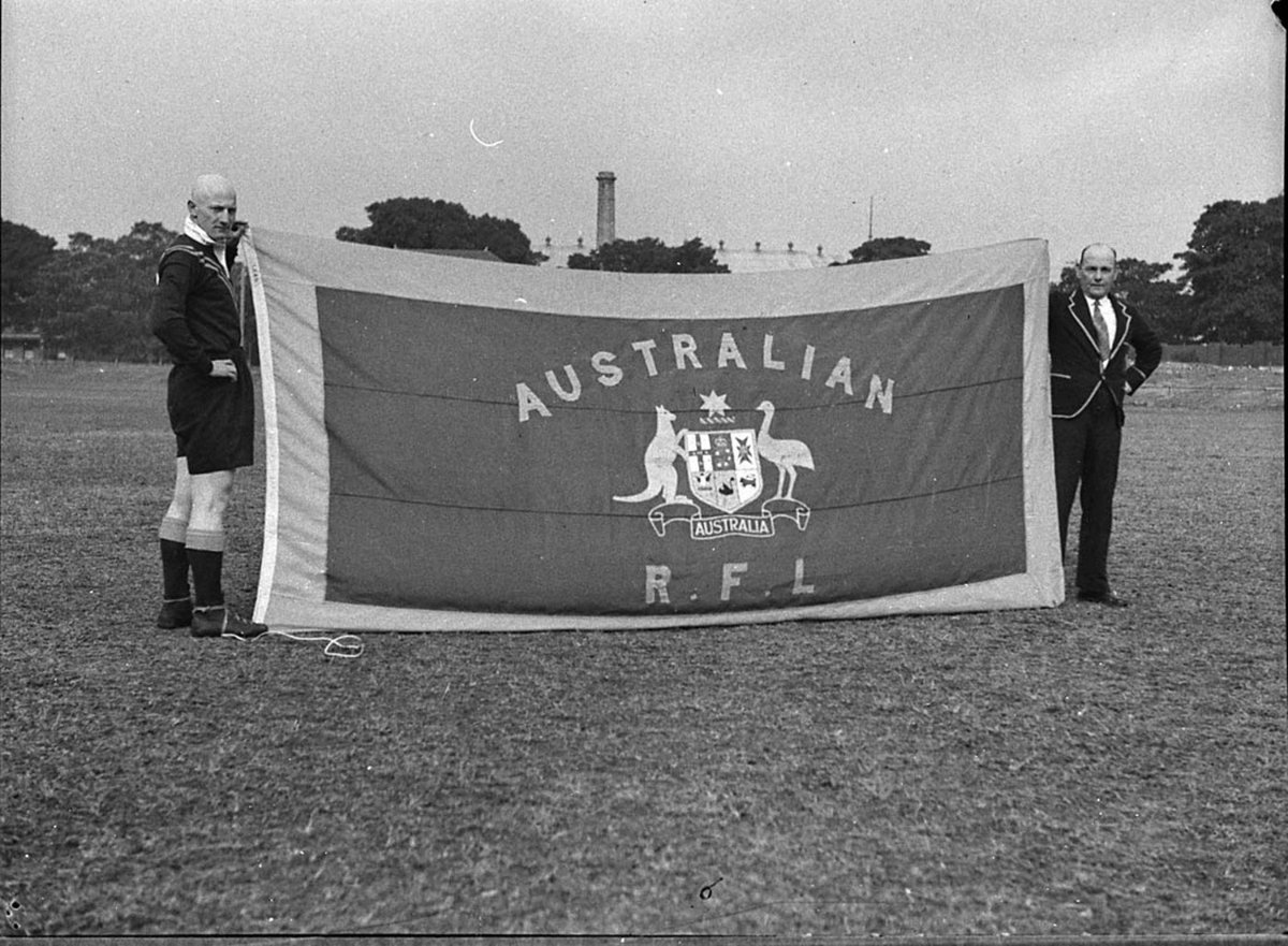 (A "Kangaroo" (Australian Rugby League Football Team member) and an official hold the team flag) SCG, c. 1930s, by Sam Hood, Moore Park