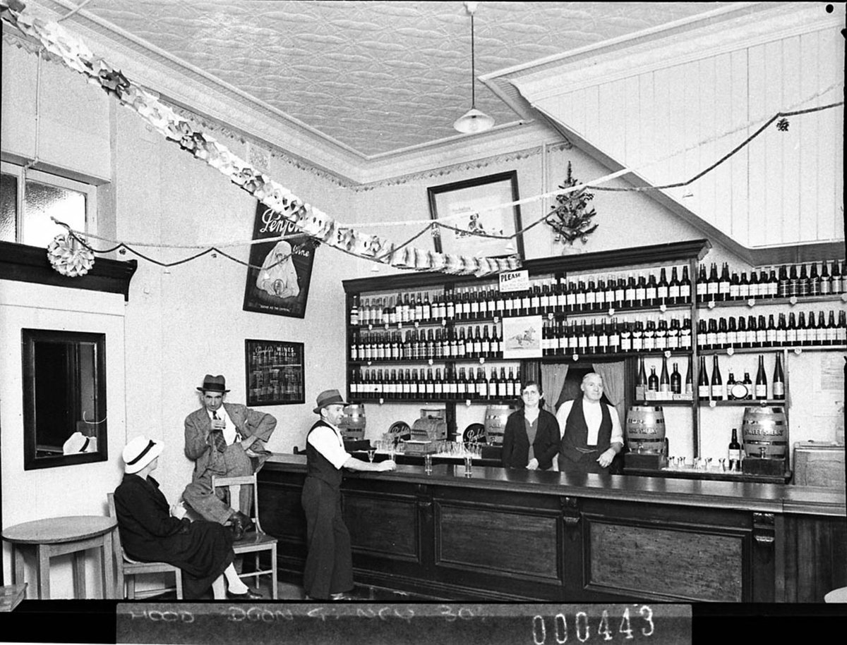 Penfold's Wines display in a wine bar; proprietor and his wife behind the bar and three customers, January 1939 by Sam Hood