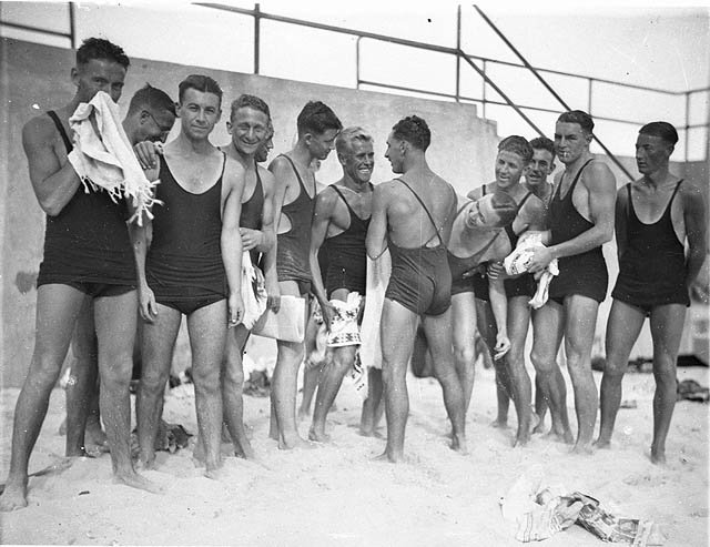 Young male surfers ("The Pier Club Mob") tease Alf "Bait" Gould about his backless swimsuit (a gift from his girlfriend), Bondi Beach, 10 October 1932, by Sam Hood