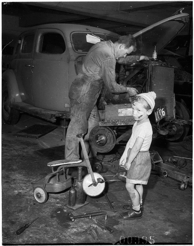 Young boy with dinky in car workshop while his father (?) services a car, Bondi, 6 October 1955 - Ern McQuillan (1955?)