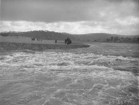 Crowds watch from the bank as Narrabeen Lake pours into the sea, 1927