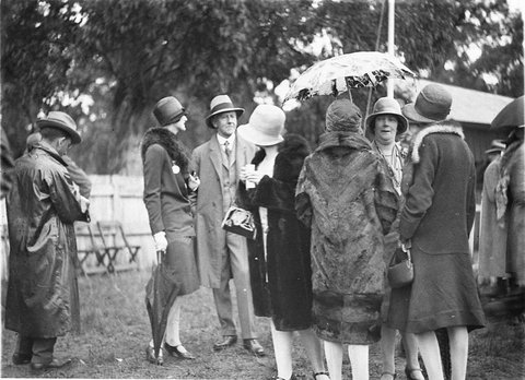 Group of racegoers in fur coats and rain gear, 1927–30