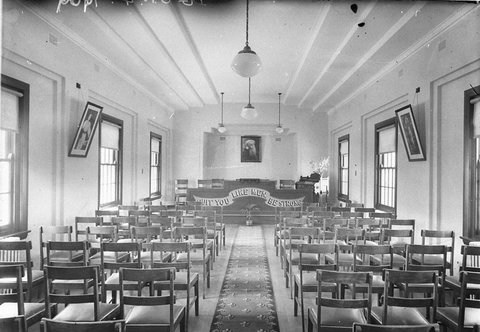 Interior of a chapel fleur de lys pattern on carpet runner and large sign on pulpit Quit You Like Men Be Strong, 1930s