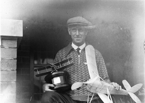Man holds a model monoplane and a trophy with a biplane, c. 1930