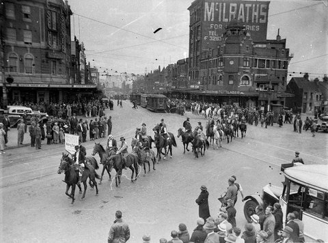 Procession of men and women pupils from the Walker Butler Riding School turning from Oxford Street into Flinders Street at Taylor Square Darlinghurst, c. 1934