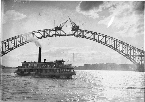 Sydney ferry Kubu passes near the Harbour Bridge as the lower chord is ready for joining, c. 1930