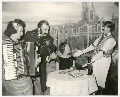 Elizabeth Connelly, TWA air hostess froom New York serenaded by head waiter with Mr and Mrs George Miller playing the violin and accordion respectively, Music Hall Restaurant, Apr 1965