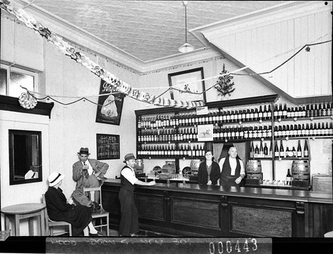 Penfold's Wines display in a wine bar; proprietor and his wife behind the bar and three customers, January 1939 by Sam Hood