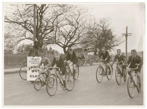 Boys of Hoyts Clovelly Theatre "Spider's Web" Club ride their bikes while "Spiderman" looks on, by Sam Hood, 1938