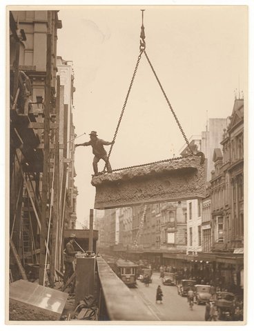 Building labourer on a stone being hoisted up to building, Pitt St, Sydney, c. 1930s, by Sam Hood