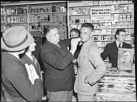 J.J. Hickey of Remington demonstrates an electric shaver on Ted Budrodeen, Mick Simmons tennis professional and coach, at Mick Simmons store, George St, Sydney, 2 October 1939, by Sam Hood