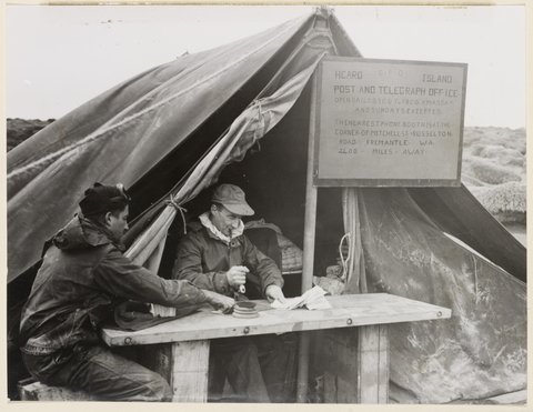 Group Captain S.A. Campbell (centre) officially opening the first Australian Post Office to be set up in Antarctica. Assistant is L. Macey, Coogee, New South Wales, Chief Radio Operator at Heard, 1950s